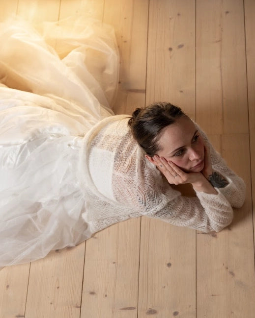 Woman lying on a wooden floor wearing the natural white Adele & Soleil Rêve V-neck cardigan and a flowing tulle skirt.