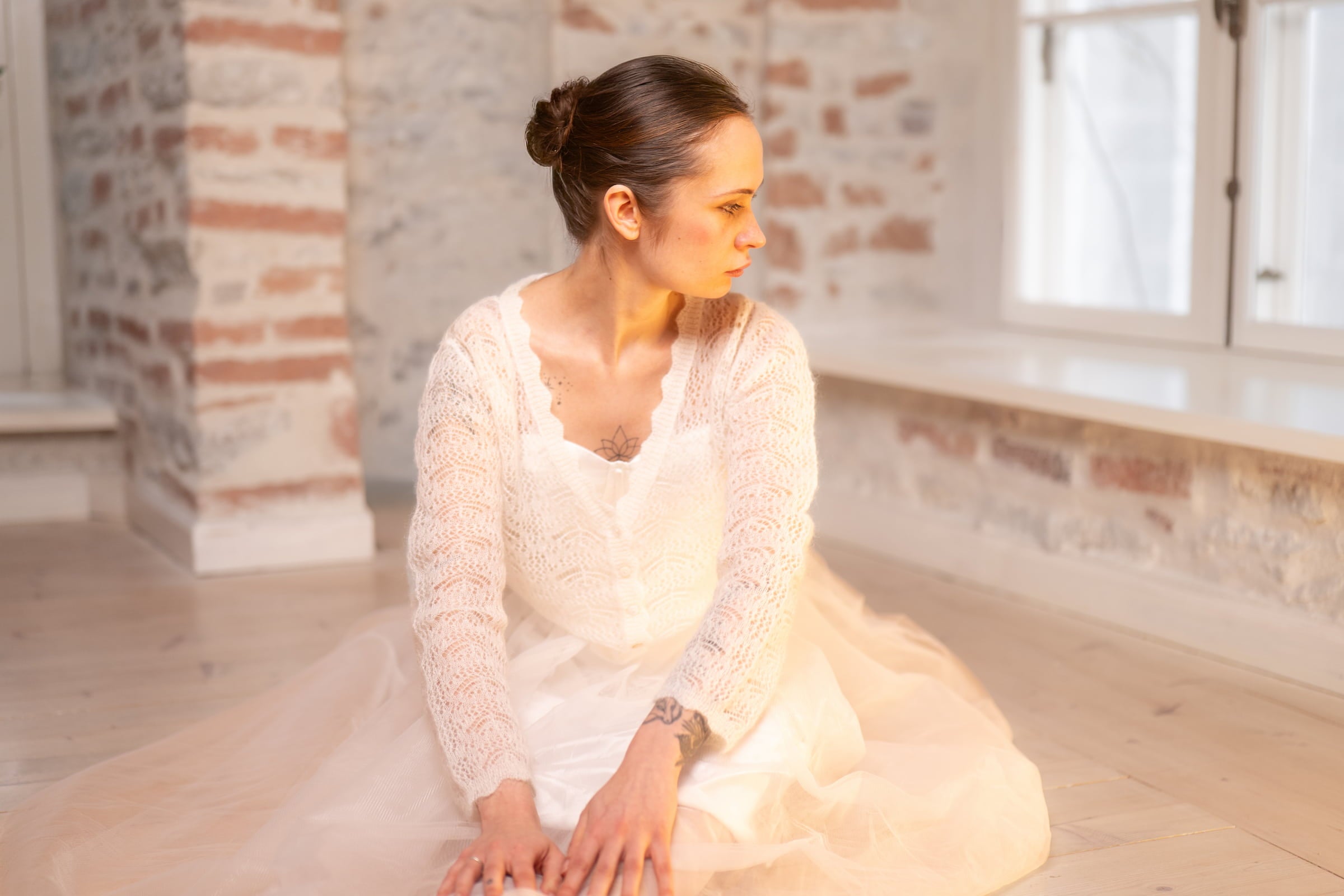 Woman wearing natural white Adele & Soleil Rêve cardigan while seated in a bright interior.