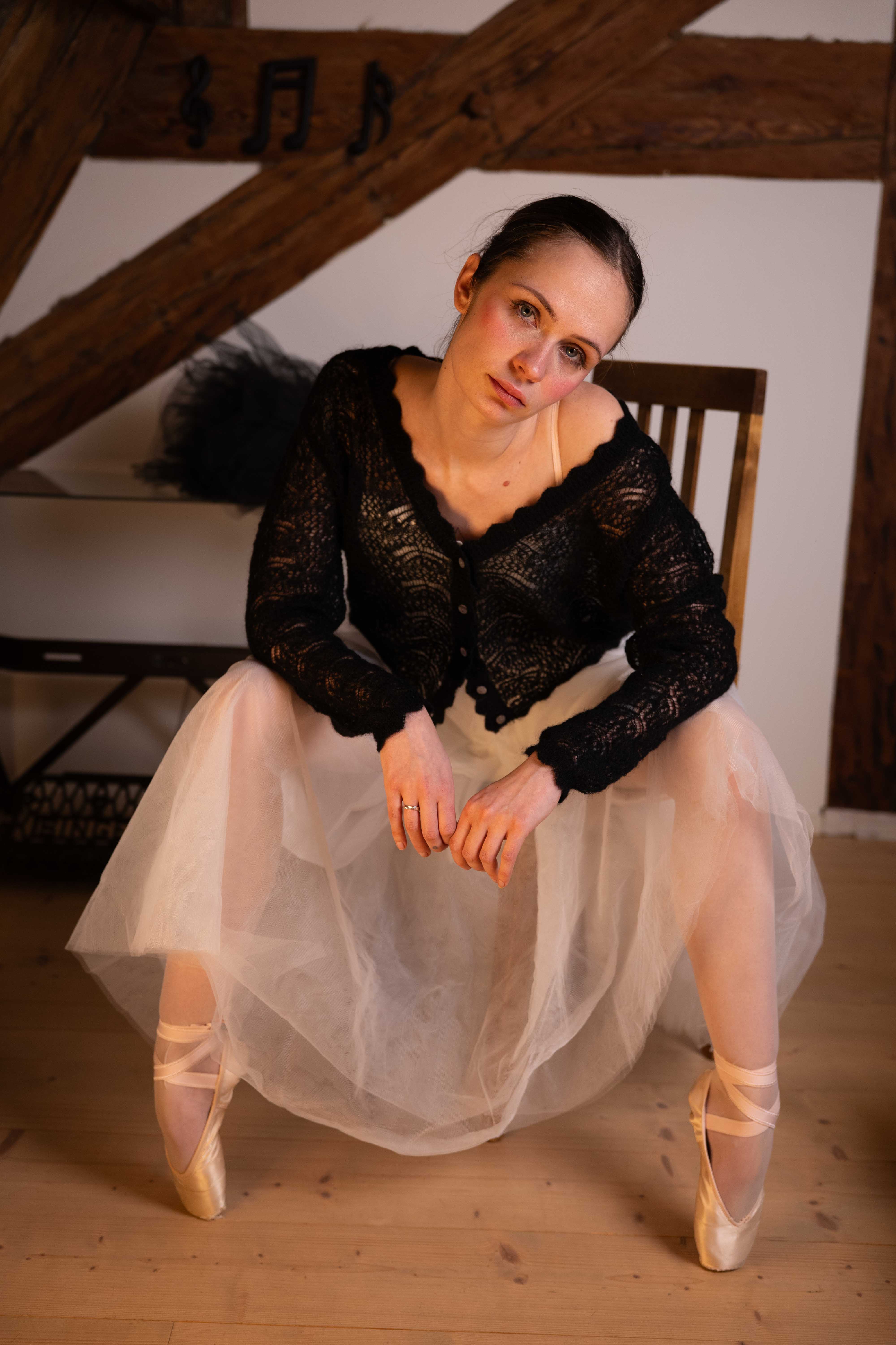 Seated woman wearing the black Adele & Soleil Rêve V-neck sweater with a flowing tulle skirt.
