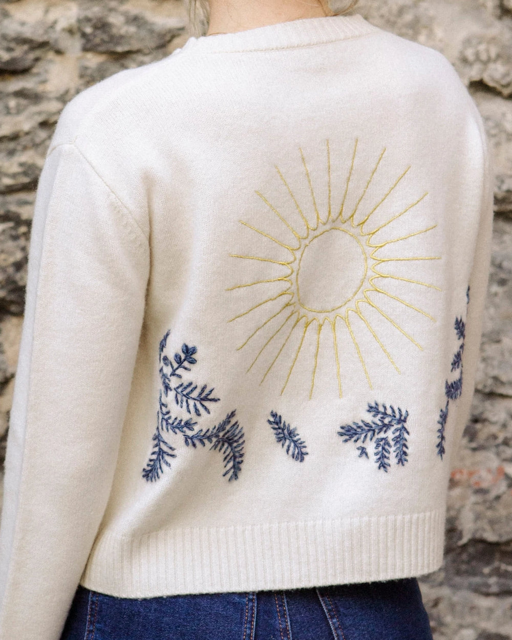Close-up of the hand-embroidered sun and floral design on the back of the natural white Adele & Soleil Jour de Soleil sweater.