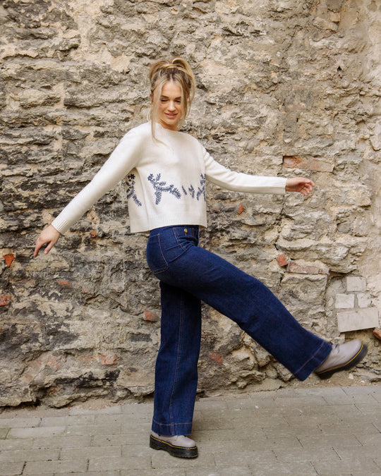 Woman wearing the natural white Adele & Soleil Jour de Soleil sweater with blue jeans, side view outdoors.