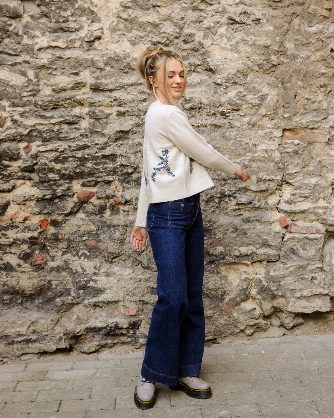 Woman wearing the natural white Adele & Soleil Jour de Soleil sweater with blue jeans, side view outdoors.