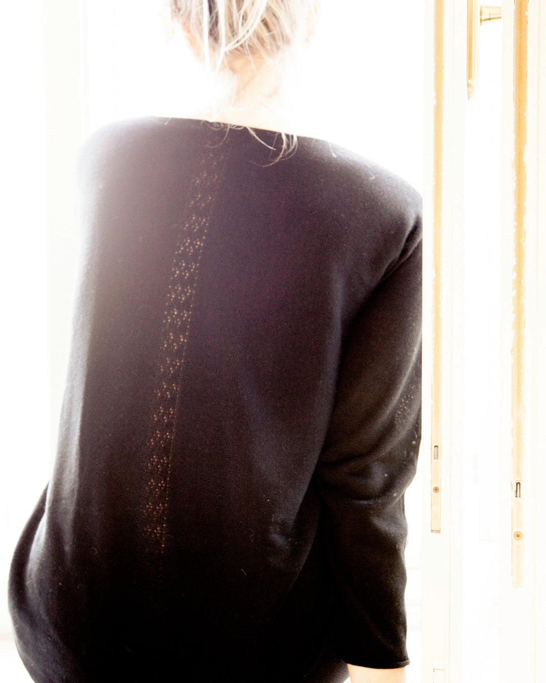 Woman wearing the black Adele & Soleil Bien-Être boat-neck sweater, back view.