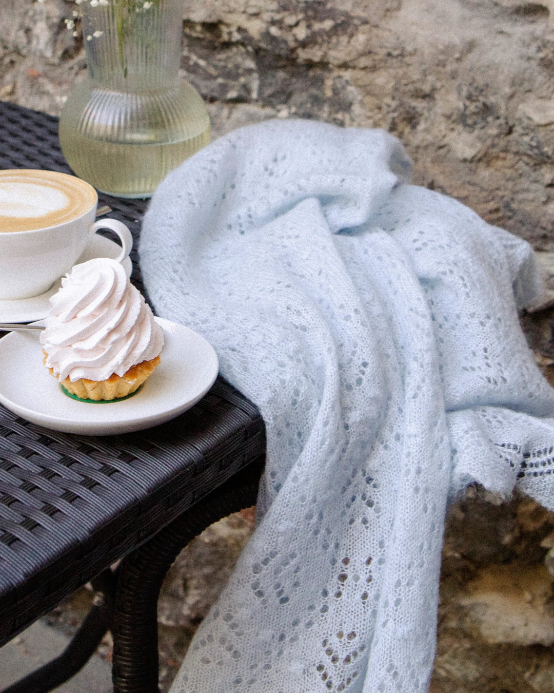 Light blue Adele & Soleil Brouillard triangle scarf draped over a woman’s shoulders at an outdoor café.