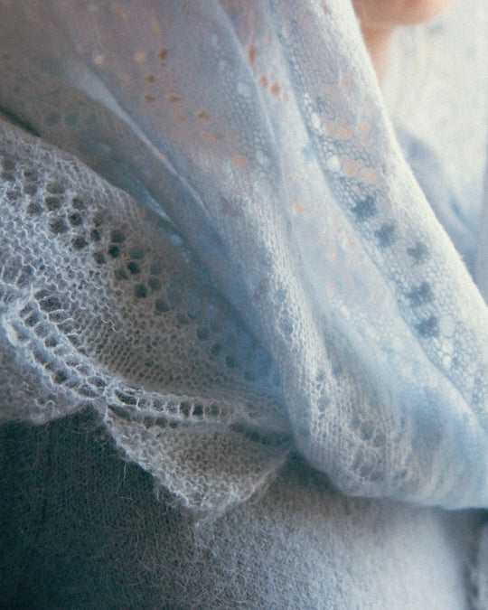 Close-up of the intricate lace-knit pattern of the Adele & Soleil Brouillard triangle scarf in light blue.