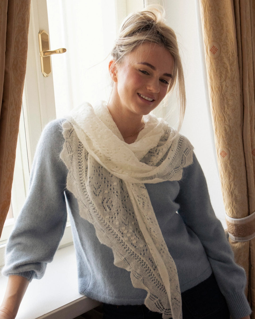Front view of a woman wearing the Adele & Soleil Brouillard natural white lace-knit triangle scarf.