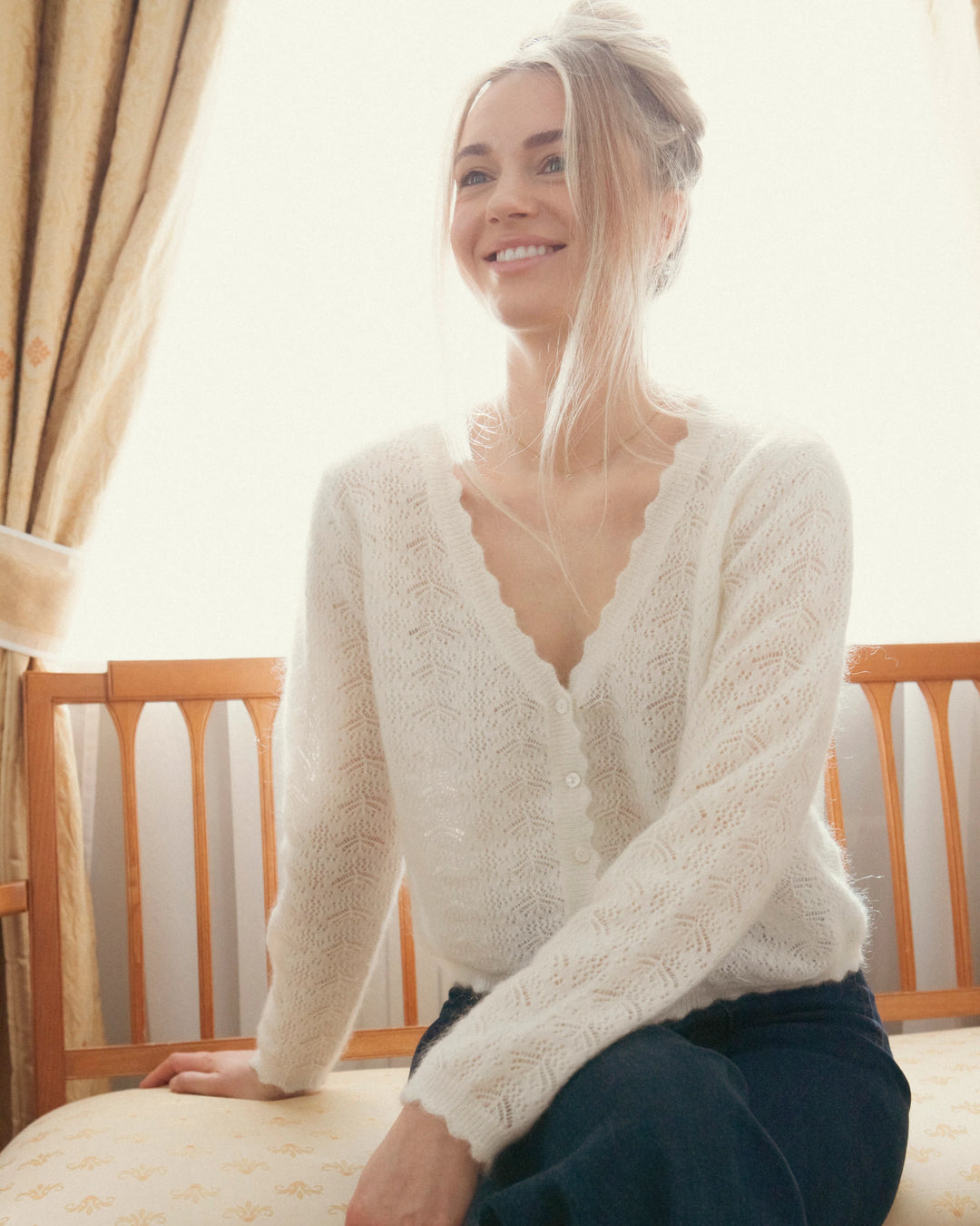 Seated woman wearing the natural white Adele & Soleil Fée V-neck knit sweater, front view.