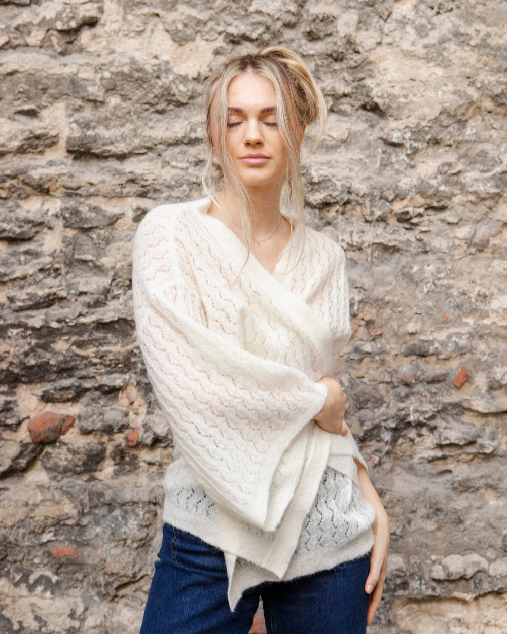 Woman wearing the Adele & Soleil Jasmin natural white wrap cardigan with wide kimono sleeves, standing against a stone wall.