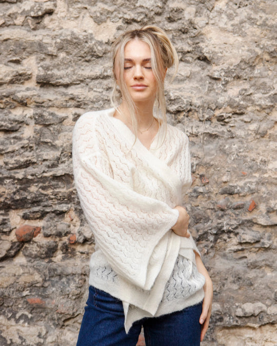 Woman wearing the Adele & Soleil Jasmin natural white wrap cardigan with wide kimono sleeves, standing against a stone wall.