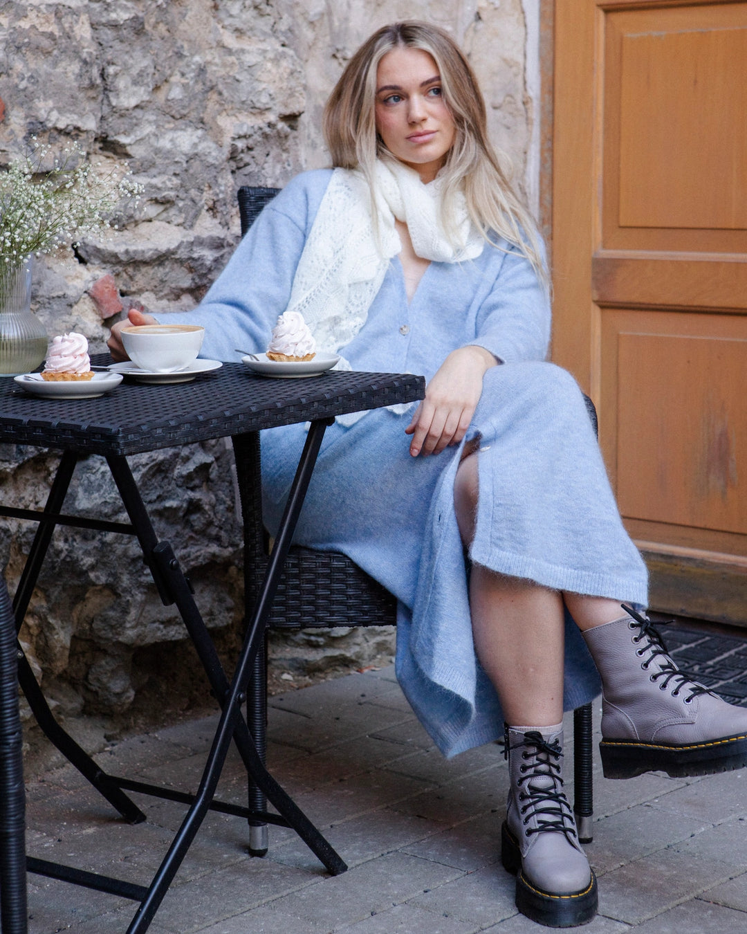 Full-length view of a woman wearing the Adele & Soleil Lundi Matin sky blue longline cardigan, seated at a café table.