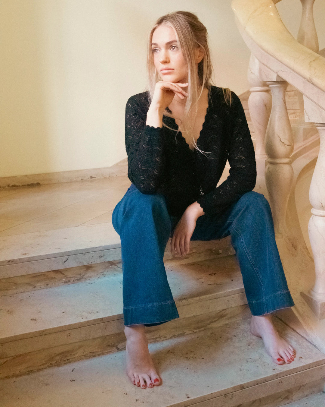 Woman wearing the black Adele & Soleil Rêve V-neck sweater with blue jeans, seated on stairs.