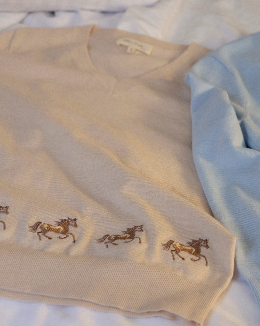 Close-up of the embroidered horse motif and soft knit texture of the Adele & Soleil Sauvage light beige sweater.