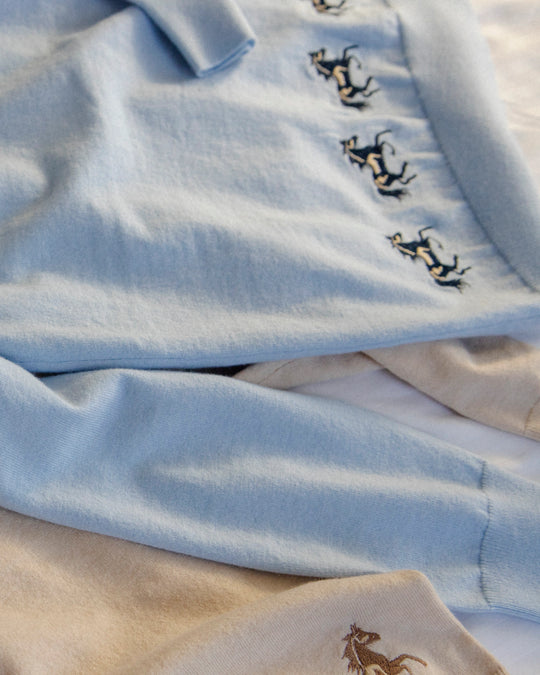 Close-up of the embroidered horse motif and soft knit texture of the Adele & Soleil Sauvage light blue sweater.