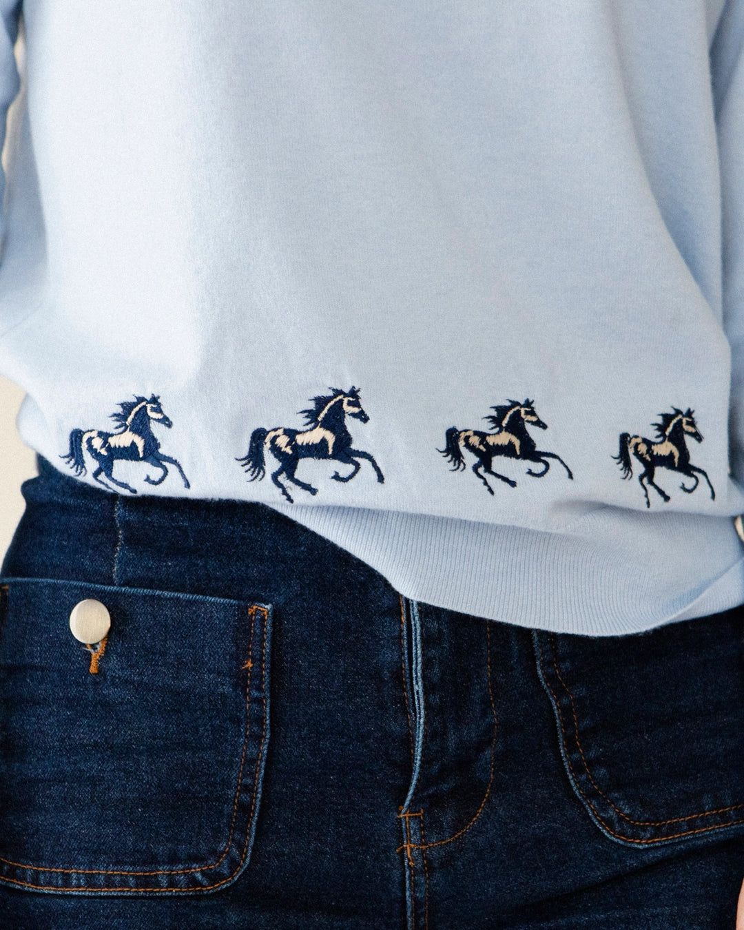 Embroidered horse detail on the light blue Adele & Soleil Sauvage sweater.