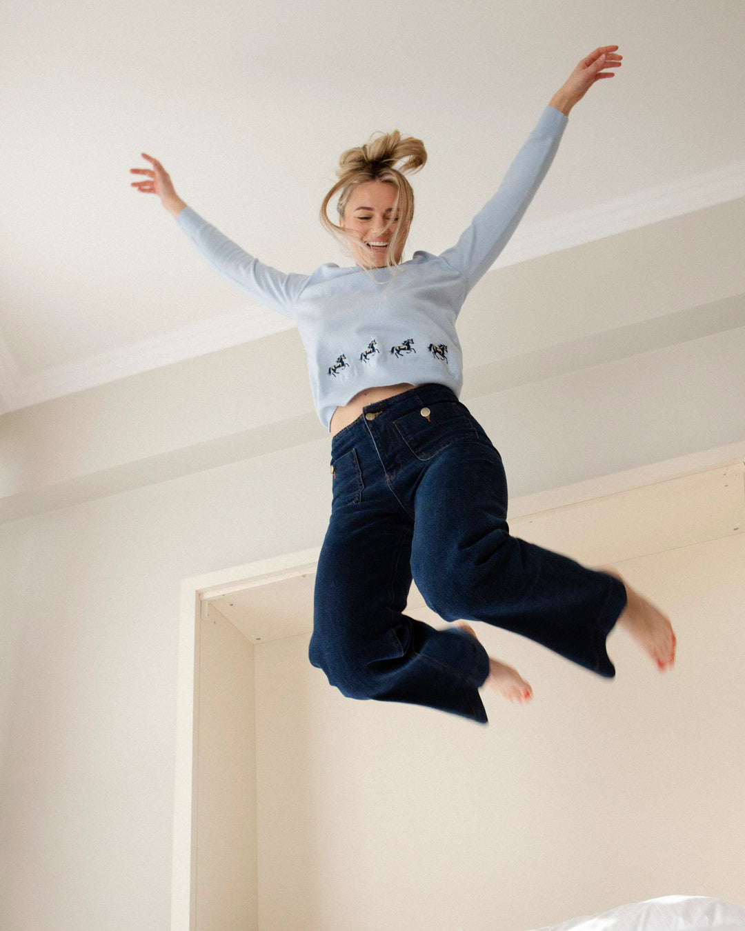 Woman wearing the Adele & Soleil Sauvage light blue V-neck sweater, jumping indoors.