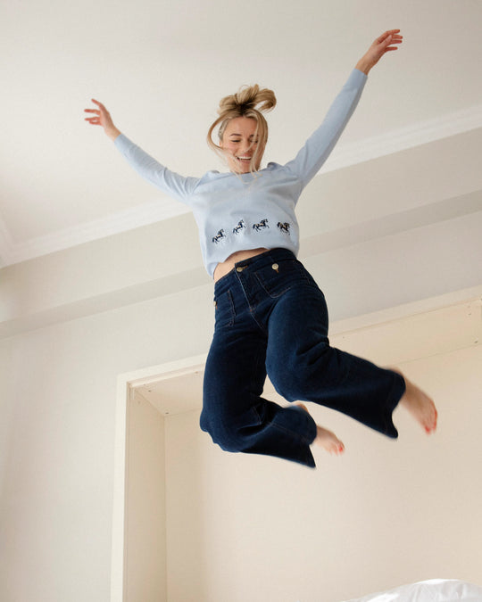 Woman wearing the Adele & Soleil Sauvage light blue V-neck sweater, jumping indoors.
