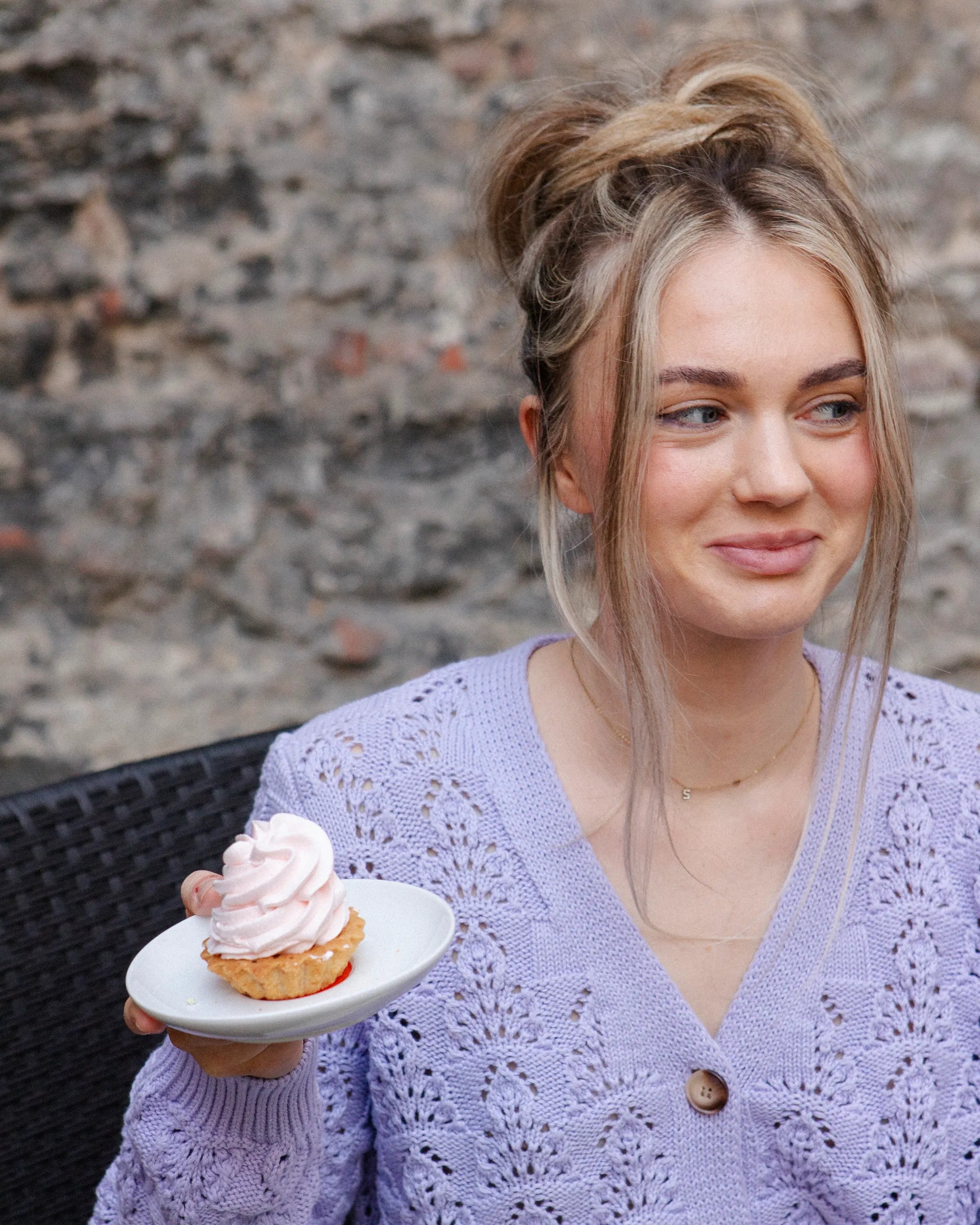 Woman seated with a cupcake while wearing the Adele & Soleil Sérène lavender textured cotton cardigan.