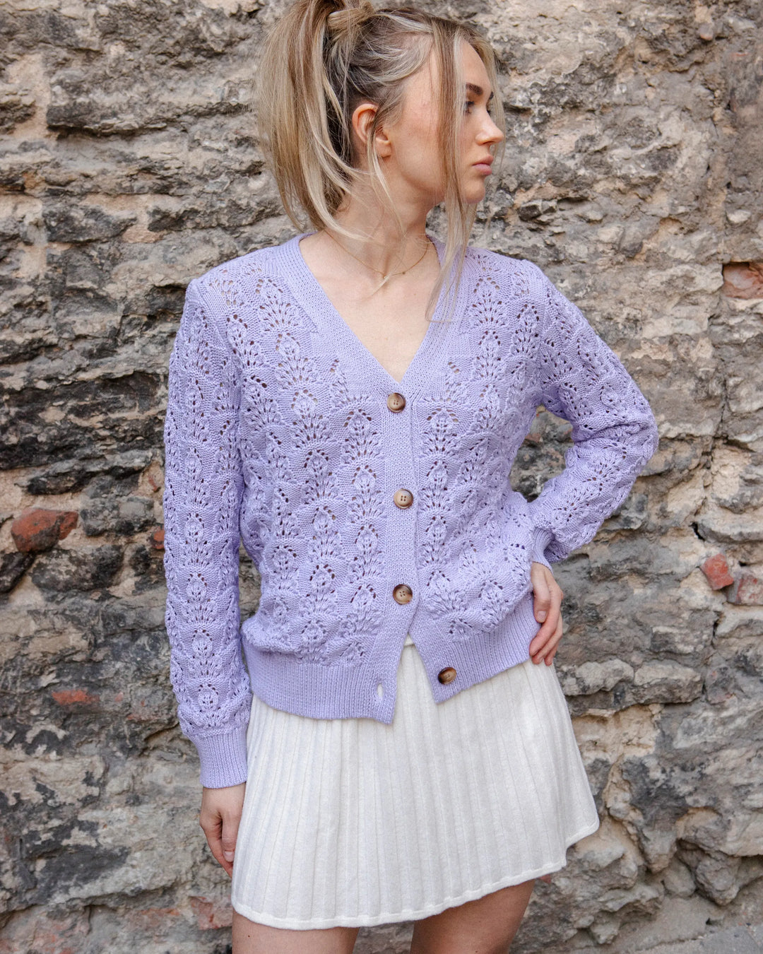 Woman wearing the Adele & Soleil Sérène lavender 100% cotton button cardigan, standing against a stone wall.