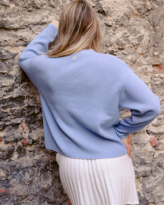 Back view of a woman wearing the Adele & Soleil Toujours sky blue merino cardigan, showing the embroidered sun detail at the neckline.