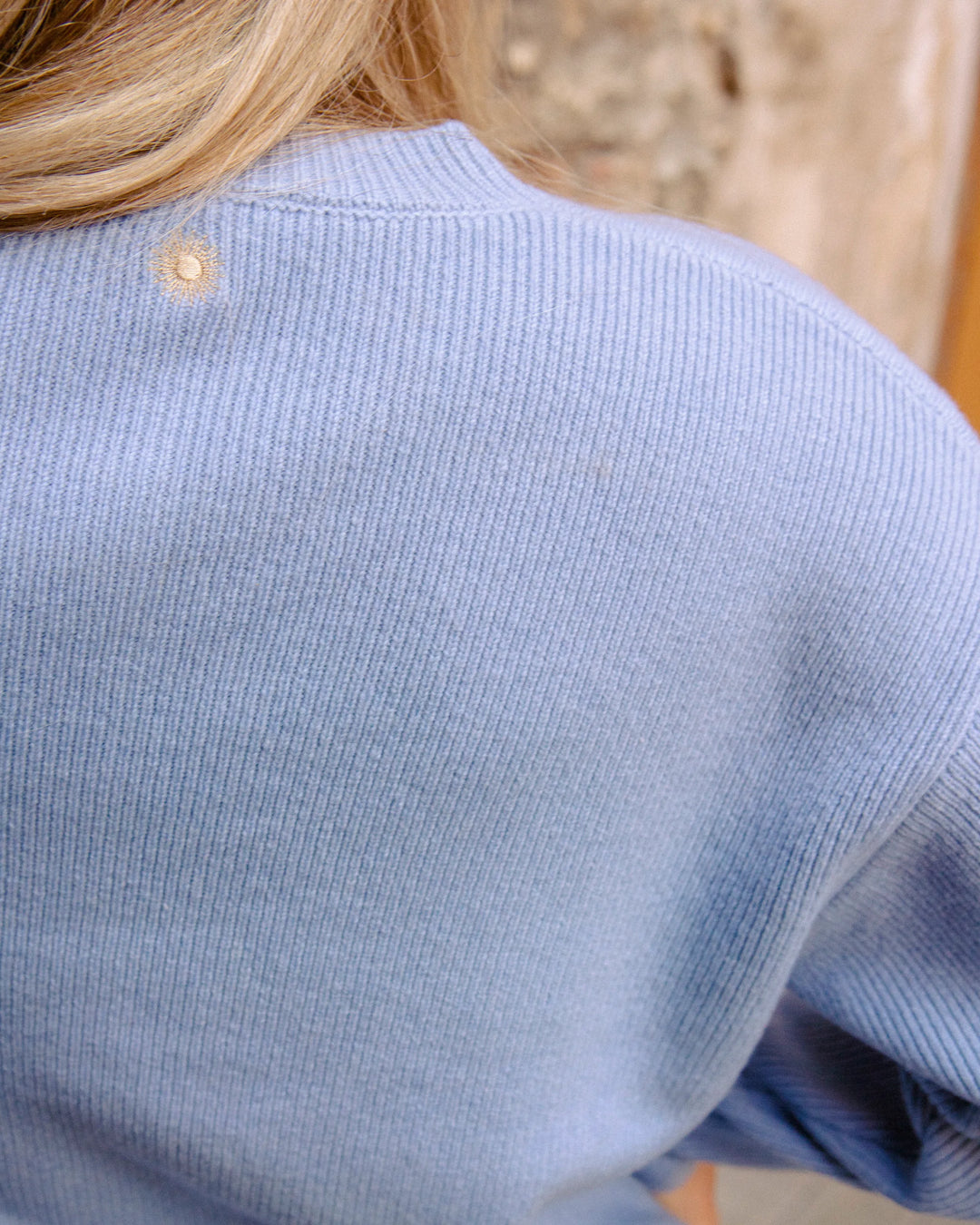 Close-up of the golden embroidered sun at the back neckline of the Adele & Soleil Toujours sky blue merino cardigan.